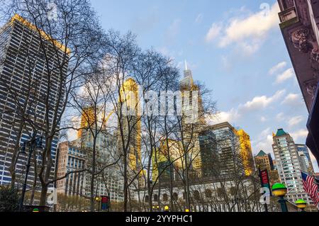 Wolkenkratzer überragen bei Sonnenuntergang in New York City über blattlosen Bäumen, mit goldenem Sonnenlicht, das von den Glasfassaden reflektiert wird. Stockfoto