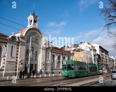 Sofia, Bulgarien; 9. Dezember 2024: Alte grüne Straßenbahn, die an einem historischen Gebäude im Stadtzentrum von Sofia vorbeifährt Stockfoto