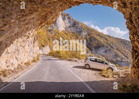 29. Oktober 2024, Piva-See, Montenegro: Weißes Auto Toyota Yaris parkt an einem natürlichen Tunnel, der in den Felsen in den Bergen gehauen wurde Stockfoto