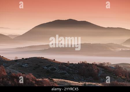 Niedrig liegender Nebel bedeckt Schichten von Hügeln bei Sonnenaufgang mit einem wunderschönen orangen Himmel Stockfoto