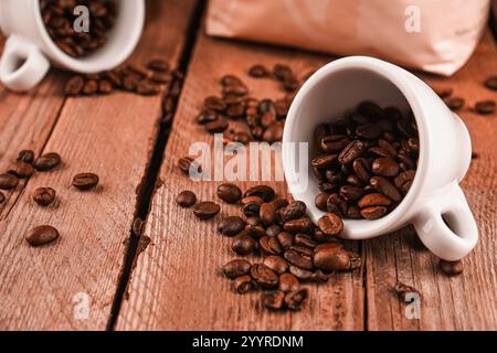 pantone-Palette. Geröstete Bohnen für den Massenverkauf. Verschüttete Kaffeebohnen aus zwei weißen Keramikbechern auf braunem Holzhintergrund. Café-Bar Stockfoto