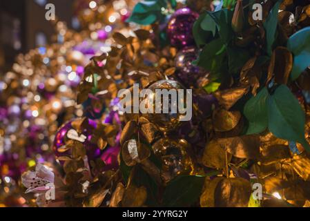 Ein lebhafter Weihnachtsbaum in London, geschmückt mit goldenen Blättern, glänzenden Kugeln in Gold und Violett und üppigem Grün, das durch warme Beleuchtung verstärkt wird. Stockfoto