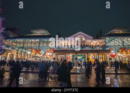 Das Covent Garden in London bietet farbenfrohe Lichter und Ornamente. Eine Menschenmenge genießt das Urlaubsambiente mit einem beleuchteten Weihnachtsbaum und kopfsteingepflasterten Straßen. Stockfoto