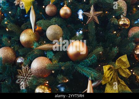 Ein üppiger Weihnachtsbaum mit goldenen und bronzenen Kugeln, Sternen und Schleifen. Kleine weiße Lichter sorgen für ein warmes Leuchten und sorgen für eine festliche Atmosphäre Stockfoto