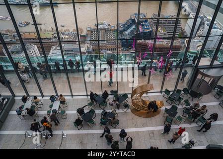 Innenblick auf den Sky Garden in London mit Menschen, einem goldenen Halbmond und rosa Sternlichtern. Die Themse und das Stadtbild sind durch große Gewinne sichtbar Stockfoto