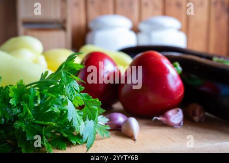Eine Vielzahl von frischem Gemüse und Kräutern ist ordentlich auf einem hölzernen Schneidebrett angeordnet. Bunte rote Tomaten, Knoblauchzehen und leuchtend grüne Petersilie Stockfoto