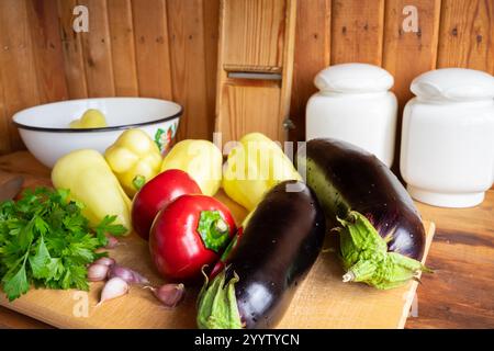 Frisches Gemüse, einschließlich Auberginen, Paprika und Knoblauch, ist ordentlich auf einer hölzernen Arbeitsplatte angeordnet. Eine Schüssel und Gewürzgläser sind im Ba sichtbar Stockfoto