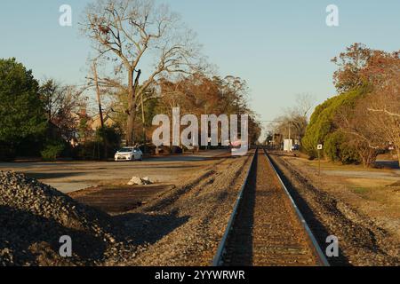 Wide View Railroad Gleise führen die Linien Harlem, GA mit Blick nach Westen auf Bäume auf beiden Seiten. Sonnenschein am frühen Morgen mit blauem Himmel. Stockfoto