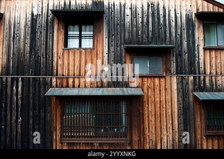 Ein Muster von Fenstern an einer verwitterten Fassade eines alten japanischen Holzgebäudes in Omihachiman, Shiga, Japan. Stockfoto