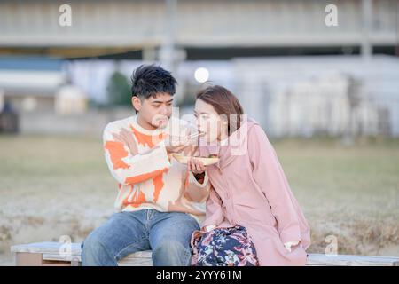 Ein japanisches Paar im Alter von 20 Jahren isst im Herbst in Tokoname, Präfektur Aichi, Takoyaki auf einer kalten und windigen Strandbank. Stockfoto