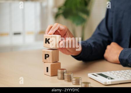 Eine Nahaufnahme eines Geschäftsmanns, der Holzwürfel hält, die KPI in der Nähe von Münzen und einem Taschenrechner buchstabieren. Steht für DIE Planung des KEY PERFORMANCE INDEXES, emplo Stockfoto