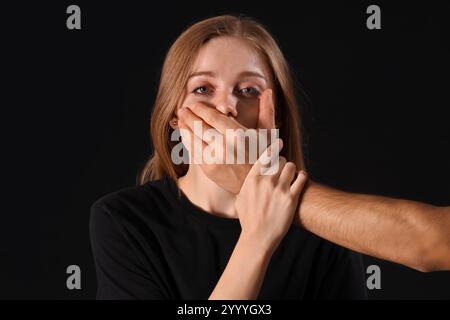 Mann, der den Mund der schreienden Frau auf dunklem Hintergrund schließt Stockfoto