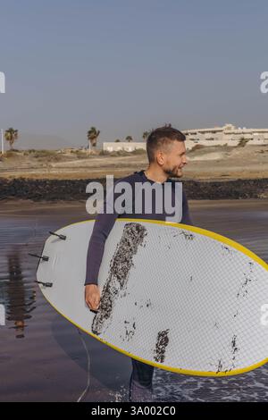 Porträt eines jungen männlichen Surfers in einem Neoprenanzug am Strand. Stockfoto