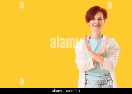 Reife Frau mit STOP-Geste auf gelbem Hintergrund. Regelkonzept Stockfoto
