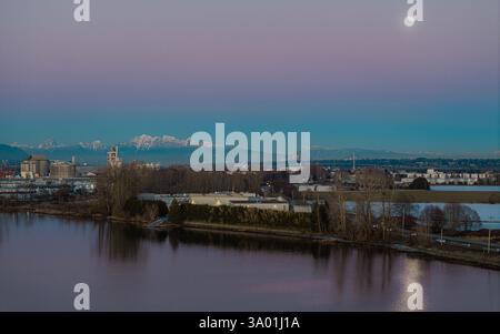 Delta BC Kanada - 11. Februar 2025: Sonnenuntergang im Deas Island Regional Park am Ufer mit Mondaufgang über dem Berg Stockfoto