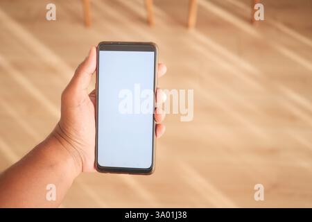 Hand hält ein leeres Smartphone mit Holzboden im Innenbereich Stockfoto