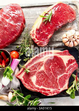 Frisches rohes Rindfleisch für köstliche saftige Steaks mit Gewürzen und Kräutern. Zubereitung für gegrilltes Fleisch auf weißem Hintergrund Stockfoto