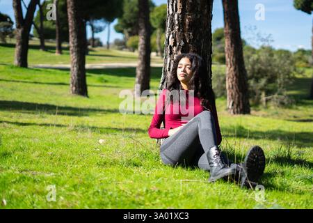 Eine ruhige junge lateinfrau, die sich an einem Baum in einem sonnigen Park ausruhen und die friedliche Atmosphäre genießen kann Stockfoto