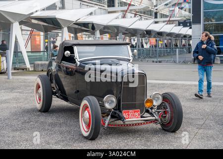 Klassischer schwarzer Roadster, der an einem sonnigen Tag außerhalb der modernen Architektur geparkt wurde und die Fans begeistert waren Stockfoto
