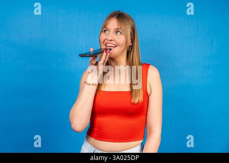 Fröhliche Frau, die den Sprachassistenten des Smartphones nutzt, Audio-Nachrichten aufnimmt oder Anrufe über die Freisprecheinrichtung tätigt Stockfoto