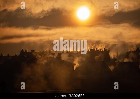 Goldener Sonnenaufgang über den Dächern des Dorfes mit Rauch aus mehreren Kaminen Stockfoto