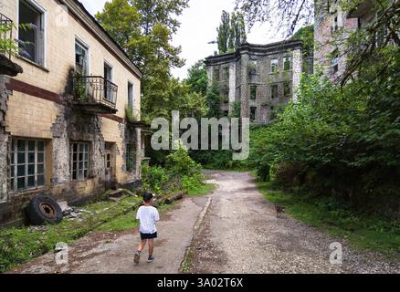 Ein Kind spaziert auf einer verlassenen Ruine in Akarmara, Tkvarcheli, Abchasien. Altes Gebäude, das im Sommer von grünem Gras bewachsen ist. Konzept von wa Stockfoto