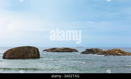 Riesige Aussicht auf das Meer mit Felsen und einem fernen Schiff unter klarem blauen Himmel in der Nähe der Küste. Stockfoto