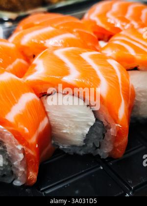 Eine Nahaufnahme frisch zubereiteter Sushi-Lachsbrötchen, die die leuchtende orange Farbe des Fisches und die zarte Textur des Reises zeigen. Stockfoto