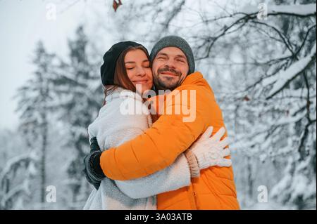 Ein nettes Paar, das sich umschließt, während es im Winterwald steht. Stockfoto