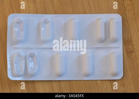 Teilweise leere Blisterpackung mit weißen Kapseln auf Holzoberfläche. Stockfoto
