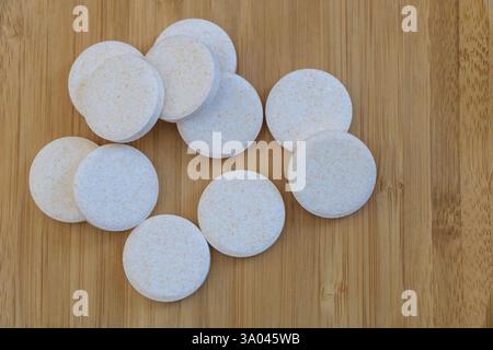 Runde weiße Pillen auf einem Holztisch, von oben gesehen. Die Pillen haben raue Kanten und winzige Flecken auf der Oberfläche Stockfoto