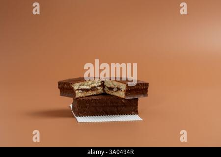 Ein köstlicher Schokoladenkuchen wird in zwei Hälften geschnitten und auf weißem Papier vor braunem Hintergrund gelegt. Der Kuchen wird in zwei Hälften geschnitten und auf ein weiteres C gelegt Stockfoto