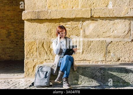 Frau, die ferngesteuert am Tablet arbeitet, während sie im Freien telefoniert. Lifestyle. Technologie. Stockfoto