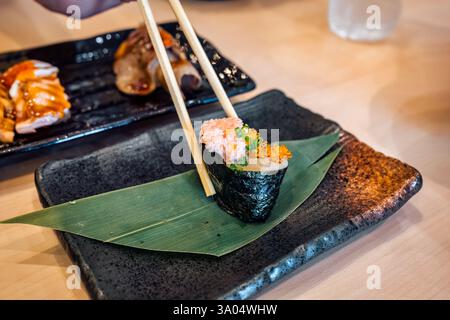 Verwenden Sie Essstäbchen, um Seetang-Sushi mit Thunfisch und Reh auf einem Keramiktablett im japanischen Restaurant aufzuheben Stockfoto