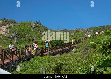 Touristen, die die hölzerne Treppe hinunter zum Strand Pontal do Atalaia steigen, umgeben von üppiger grüner Vegetation unter hellem Sommermorgen blauem Himmel. Stockfoto