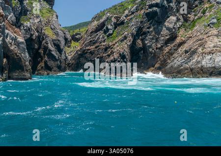 Das türkisfarbene Wasser des Atlantiks stürzt gegen die zerklüfteten Felsklippen der Insel Ilha do Farol unter einem hellen und heißen, sonnigen, klaren Himmel am Sommernachmittag. Stockfoto