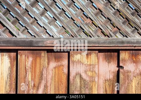 Verwitterter Holzzaun mit vertikalen Dielen und einer diagonalen Gitterplatte. Nahaufnahme. Stockfoto