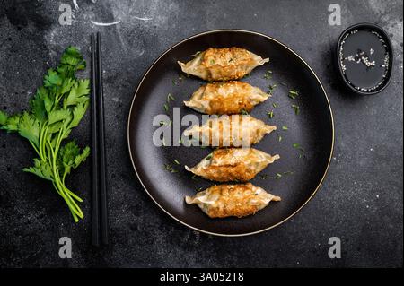 Frittierte japanische Gyoza-Knödel mit Fleisch und Gemüse auf Teller. Schwarzer Hintergrund. Draufsicht. Stockfoto