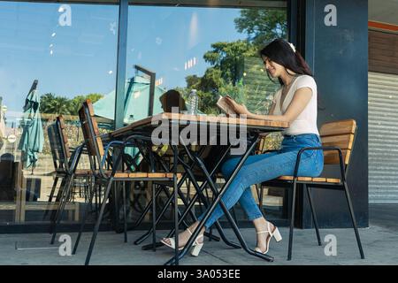 Junge hispanische Frau, die gerne Menü liest, während sie an einem Tisch in einem Café im Freien sitzt Stockfoto