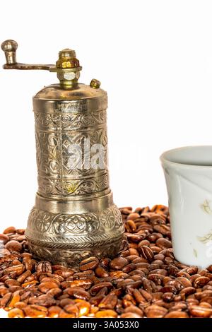 Vintage-Handkaffeemühle mit kunstvollem Metalldesign und weißer Porzellanschale auf gerösteten Kaffeebohnen Stockfoto