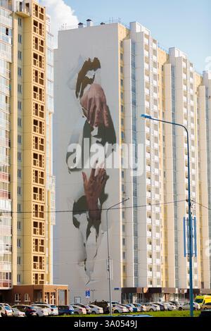 Trompe l'oeil-Wandbild mit Händen, die durch die weiße Oberfläche an der Seite des Wohngebäudes brechen Stockfoto