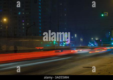Leichte Wege von fahrenden Autos auf einer verschneiten Stadtstraße bei Nacht Stockfoto