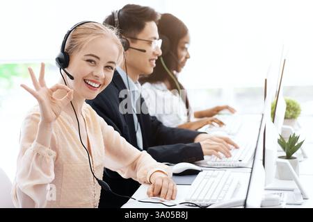 Die Kundendienstmitarbeiters zeigen eine gute Geste und ihre Kollegen arbeiten im Call Center Stockfoto