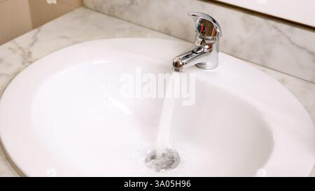 Wasser lief vom Wasserhahn in das weiße Waschbecken im Bad Stockfoto