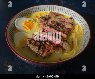 Ramen garniert mit saftigem Lendensteak, Udon-Nudeln und einem hart gekochten Ei. Stockfoto