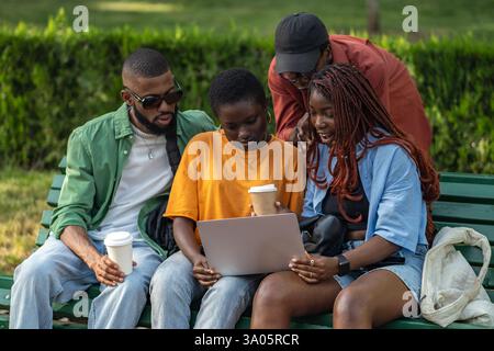 Fröhliche Gruppe afroamerikanischer Freunde trinken Kaffee und arbeiten an Laptops im Green Park Stockfoto