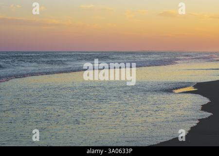 Das Abendlicht reflektiert die ruhigen Meereswellen, die über den Strand strömen. Stockfoto