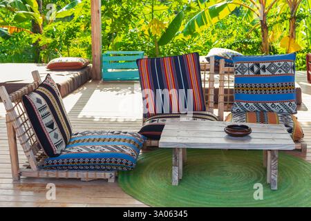 Liegestühle mit Kissen und Holztisch auf der Terrasse. Gemütliche Terrasse im Hotelresort. Leere Touristenvilla. Außendesign eines tropischen Hotels Stockfoto