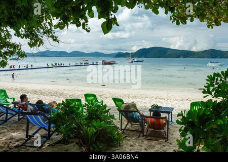 Touristen in Ruhesesseln am Strand einer thailändischen Insel in der Andamanensee und einem schwimmenden Pier Stockfoto