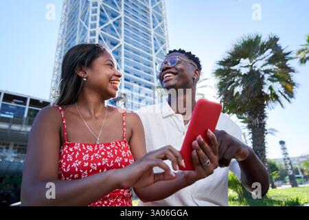 Ein junges afroamerikanisches Paar, das in den Sommerferien gemeinsam mit dem Smartphone draußen sitzt. Stockfoto